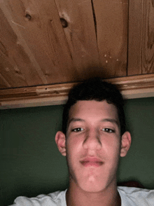 a young man is laying under a wooden ceiling and making a funny face