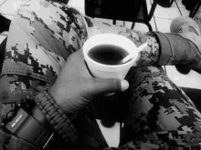 a person in a camouflage uniform is holding a cup of coffee with a spoon in it .