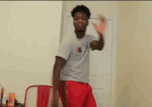 a young man in a white shirt and red shorts is standing in front of a red chair in a room .