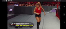 a woman in a red tank top and black shorts is walking down a wrestling ring