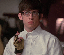 a man wearing glasses and a white shirt holds a pair of gloves around his neck