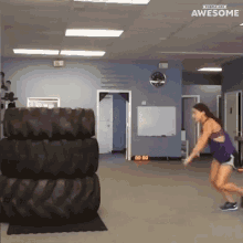 a woman is jumping over a pile of tires in a gym with the word awesome on the bottom right