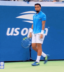 a man in a blue shirt and white shorts stands on a tennis court in front of a us open sign