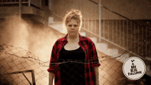 a woman in a red plaid shirt stands behind a barbed wire fence with a sign that says a mi kis falunk