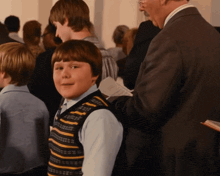 a boy wearing a striped vest is standing in a crowd