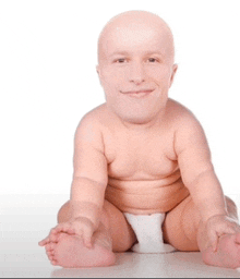 a baby without a shirt is smiling while sitting on a white surface