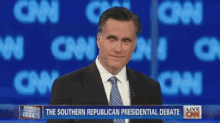 a man in a suit and tie stands in front of a cnn screen that says the southern republican presidential debate