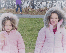 two girls wearing pink jackets with fur hoods are standing next to each other