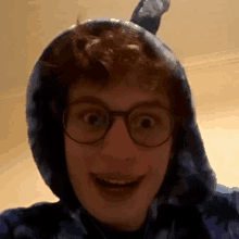 a young man wearing glasses and a blue tie dye hoodie is smiling