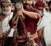 a man with a mustache is holding a rope in his hands while standing in front of a crowd of people .