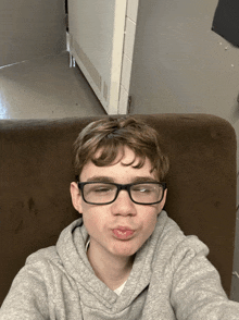 a young boy wearing glasses and a grey hoodie is making a face