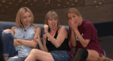 three women are sitting on a couch with one wearing a t-shirt that says ' nc ' on it