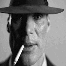 a man wearing a hat and smoking a cigarette in a black and white photo .