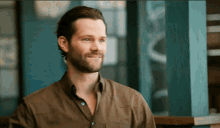 a man with a beard is smiling in front of a window
