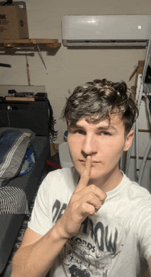 a young man wearing a white shirt with the word now on it holds his finger to his mouth