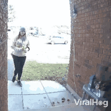 a woman is walking down a sidewalk in front of a brick building with viralhog written on the bottom right