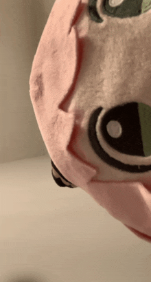 a close up of a stuffed animal with a green eye and pink hair