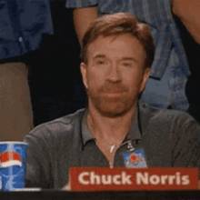 chuck norris is sitting at a table with a red sign that says chuck norris .