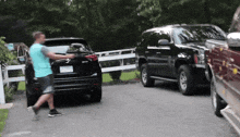 a man in a blue shirt is standing next to a black suv with a license plate that says ' jc '