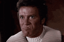 a close up of a man making a funny face while wearing a white sweater .