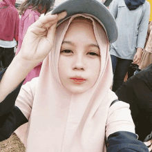 a girl wearing a hijab and a hat is taking a selfie with her hand on her hat .