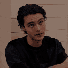 a young man in a black shirt is sitting in front of a white tile wall .