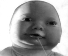 a black and white photo of a baby with a string sticking out of his mouth