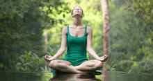 a woman in a green tank top sits in a lotus position