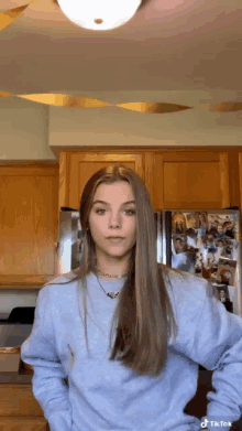 a woman in a blue sweater is standing in front of a refrigerator .