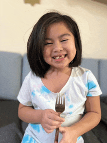 a little girl is holding a fork and smiling for the camera