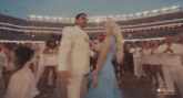 a woman in a blue dress is dancing with a man in a white suit in a stadium with the words music on the bottom