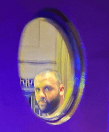 a man with a beard is reflected in a round window on a purple wall