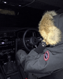 a person wearing a grey canada goose jacket is sitting in a car