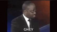 a man in a suit and tie is standing in front of a microphone and says ghey .
