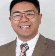 a man wearing glasses , a suit and tie is smiling for the camera .