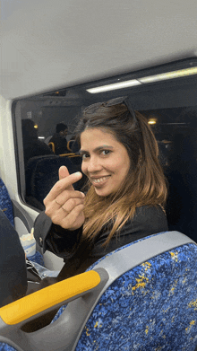 a woman sitting on a bus making a heart with her finger