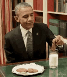 a man in a suit is sitting at a table with a plate of cookies and a glass of milk