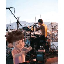 a man is playing drums while a little girl stands behind him