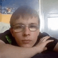 a young man wearing glasses is laying down with his hand on his shoulder .