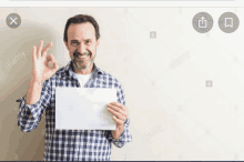 a man in a plaid shirt is holding a piece of paper and giving the ok sign