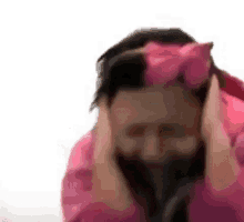 a man wearing a pink jacket and a pink bow on his head is covering his ears with his hands .