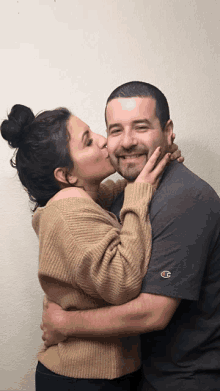 a woman kisses a man on the cheek while he wears a champion shirt