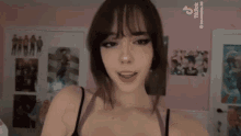a girl in a black bra is standing in front of a wall with posters on it .