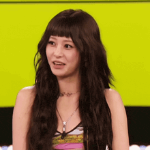 a woman with long hair and bangs is wearing a necklace with the letter t on it