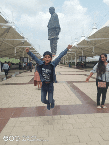 a boy jumping in front of a statue with a triple camera