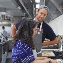 a man and a woman are cooking in a kitchen and the woman is wearing a blue shirt that says ' sally '