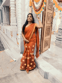 a woman in an orange polka dot saree stands in front of a temple