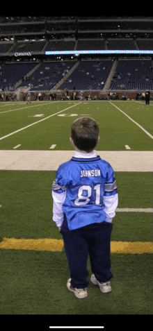 a young boy wearing a blue johnson jersey stands on a field