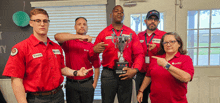 a group of people wearing red shirts with liberty on them pointing at a trophy