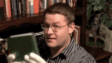 a man wearing glasses is holding a book in front of a bookshelf that has a book called the third edition